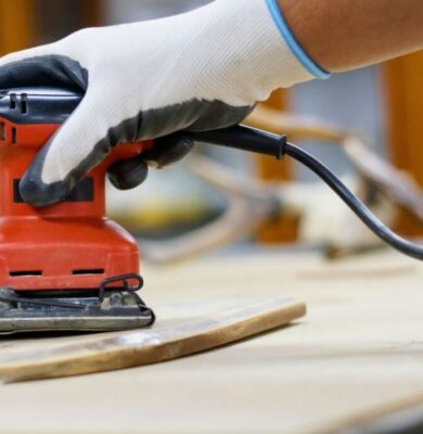 A man is sanding drywall with an electric sander.