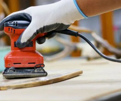 A man is sanding drywall with an electric sander.