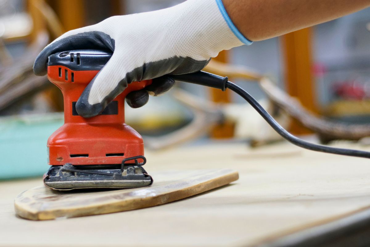 A man is sanding drywall with an electric sander.