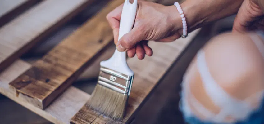 A man paintaing stain on a wooden crate.