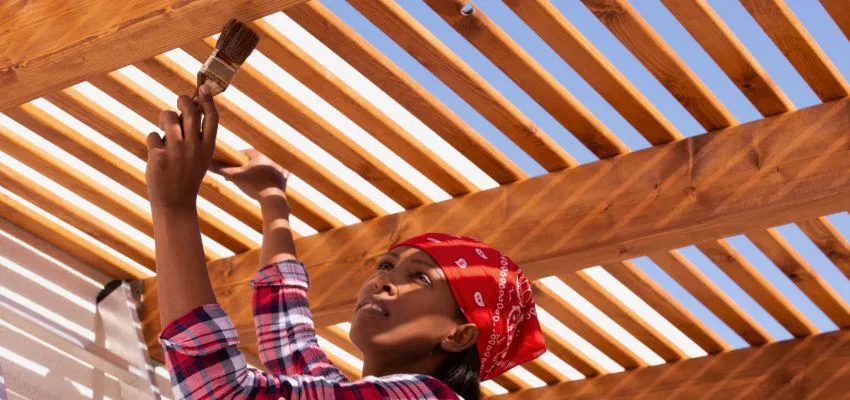 A woman applying stain on a newly installed window pergola.