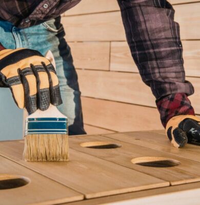 Person wearing gloves applying wood sealer with a brush on an outdoor wooden project