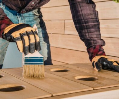 Person wearing gloves applying wood sealer with a brush on an outdoor wooden project