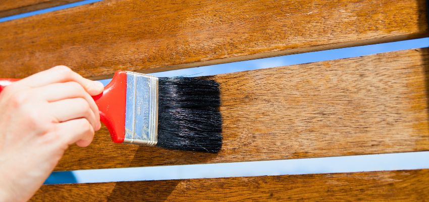 Hand applying wood sealer with a paintbrush on stained wooden planks