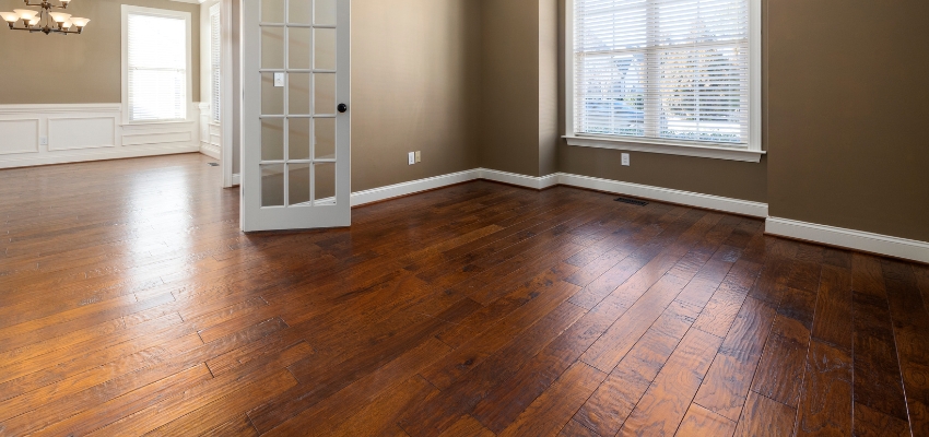 Spacious empty room with elegant dark wood floor colors in a rich chestnut tone, complemented by neutral walls and classic white trim