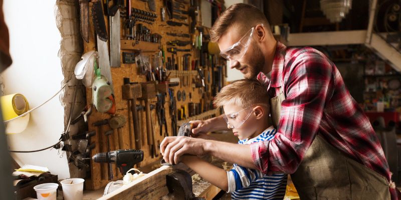 The man teaches the kid in woodworking.