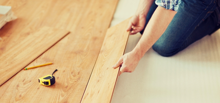 Person installing light wood flooring planks with tools, demonstrating practical wood floor identification during home renovation.