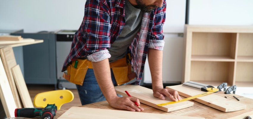 Carpenter measuring light wood boards while considering the pros and cons of rubberwood for furniture.