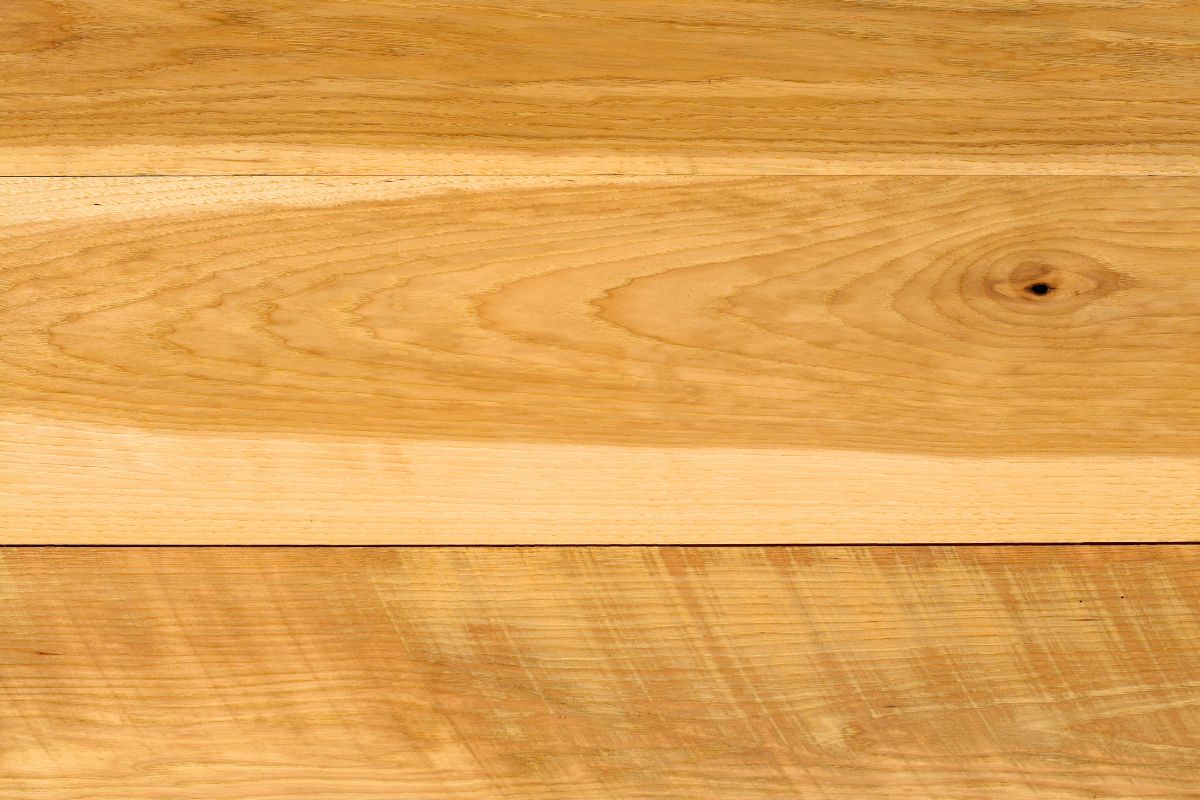 Detailed macro view of smooth, light-toned hickory wood surface showing rich grain patterns, natural knots, and warm golden hues characteristic of premium hickory wood.
