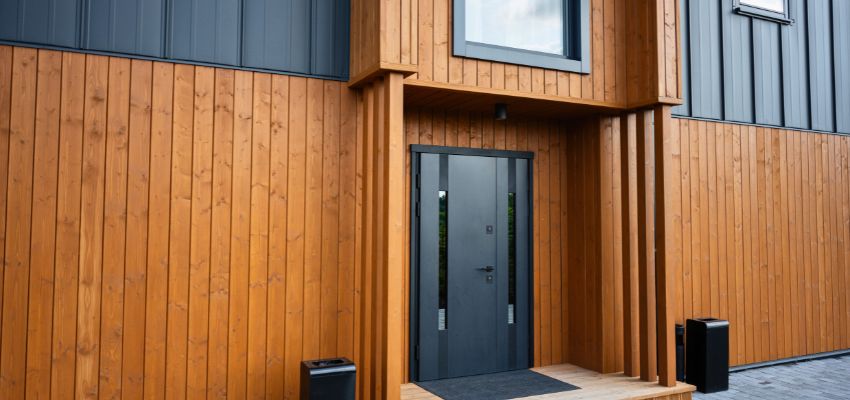 Modern building entrance featuring warm vertical wood siding and dark gray door