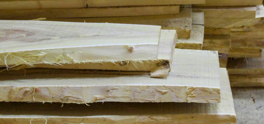 Close-up of stacked untreated wood planks showing natural grain, rough edges, and light natural color.