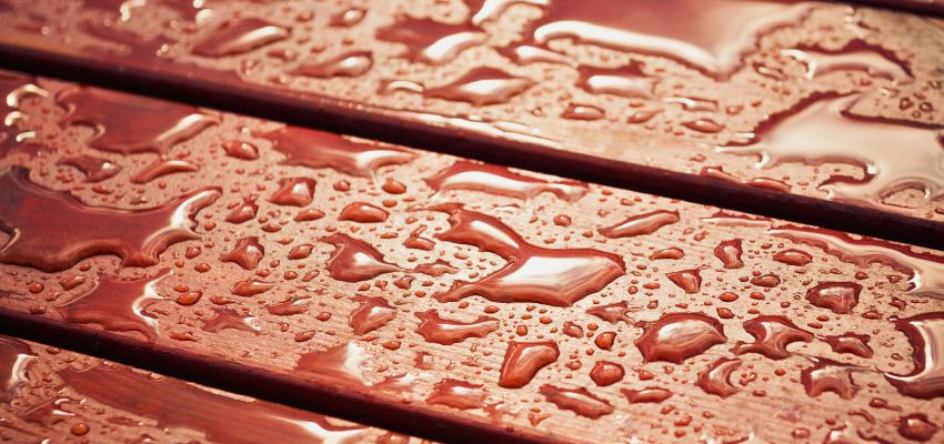 Water droplets resting on the surface of dark untreated wood, highlighting its natural texture and water resistance.